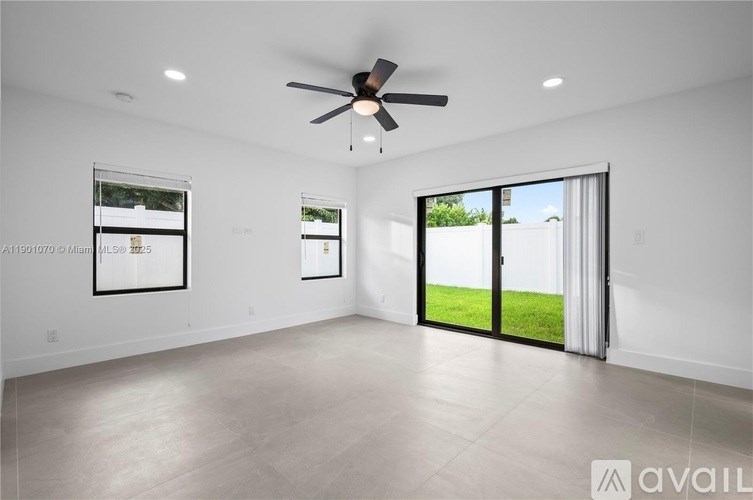 A spacious room with a ceiling fan and sliding glass doors leading to a green outdoor area.