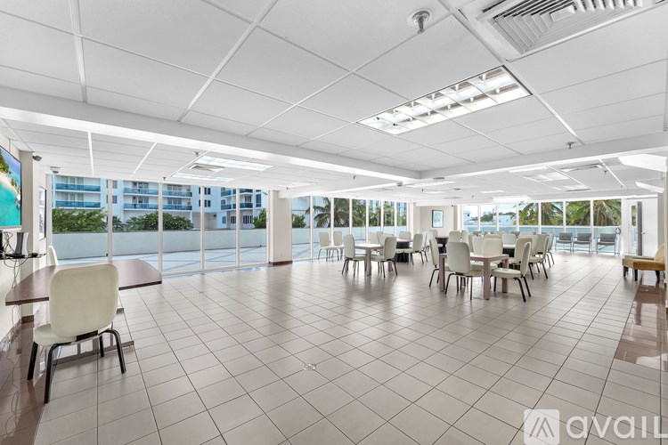 A spacious room with white chairs and tables, large windows, and a view of a cityscape.
