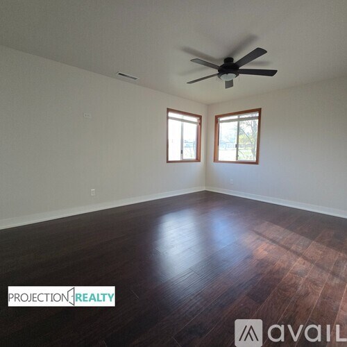A room with a ceiling fan and two windows.