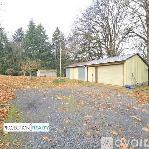 A gravel driveway leads to a garage and a small shed in a wooded area.