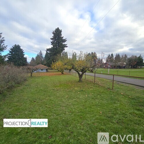 A grassy field with a fence and trees in the background.