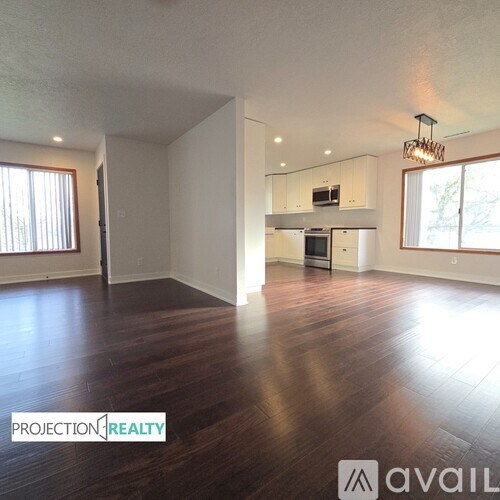 A spacious room with wooden floors and a kitchen area in the background.