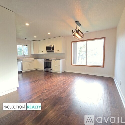 A well-lit, spacious kitchen and living room with wooden floors and white walls.