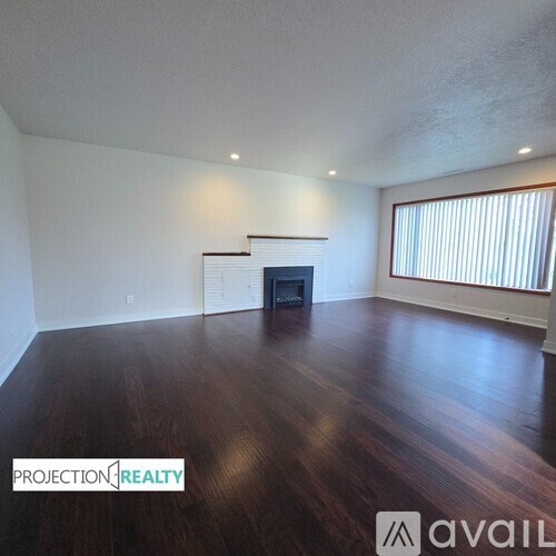 A spacious room with wooden floors and a fireplace.