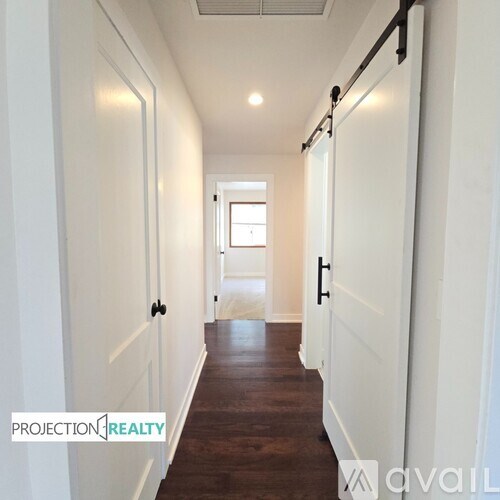 A long hallway with white doors and a window in the distance.