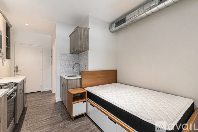 A bedroom with a bed, nightstand, and a kitchen area.