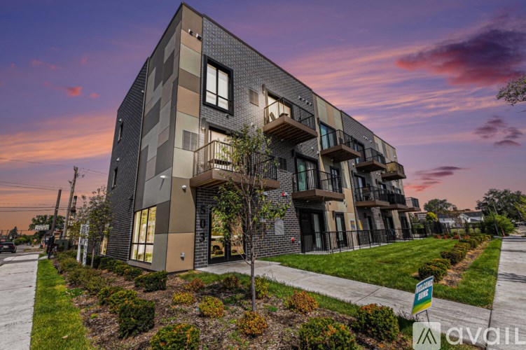 A modern multi-story building with balconies and a lawn in front.