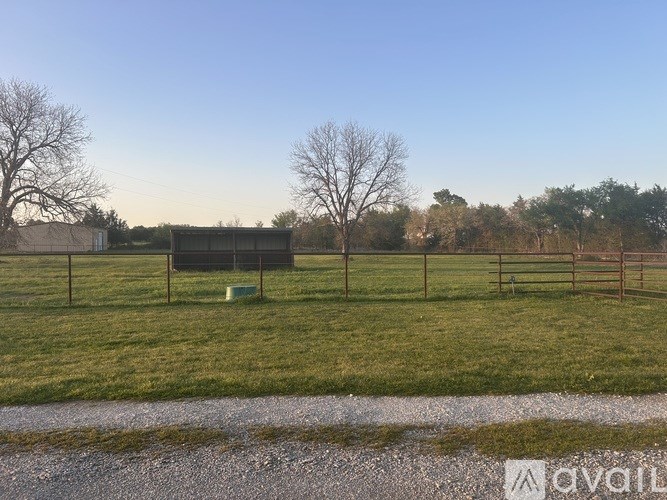 A grassy field with a fence and a building in the background.