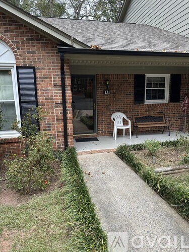 A white chair is on the porch of a brick house.