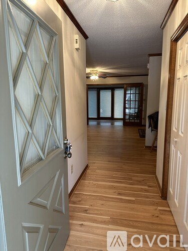 A hallway with a wooden floor and a white door with a diamond pattern on it.