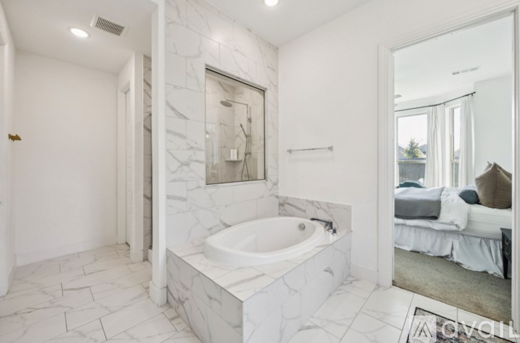 A white bathroom with a marble tub surround and a mirror.