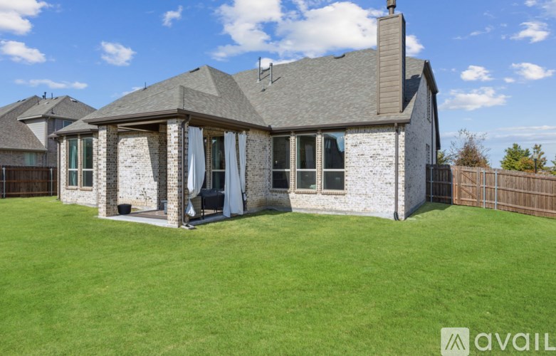 A house with a stone facade and a grey roof is surrounded by a green lawn.