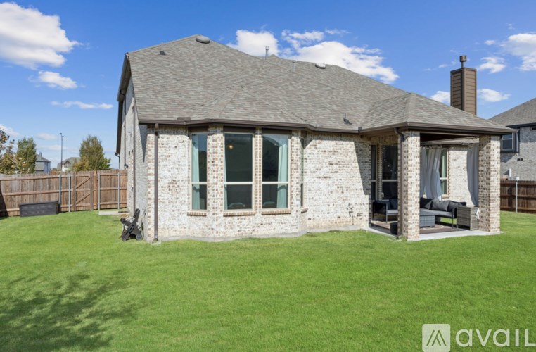 A house with a stone exterior and a grey roof is surrounded by a grassy lawn.
