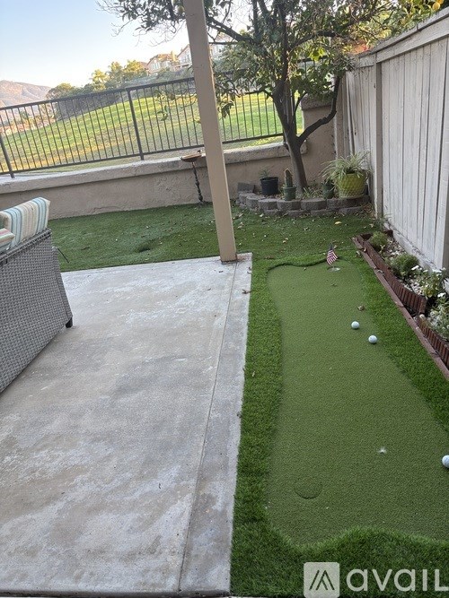 A backyard with a putting green and a patio.