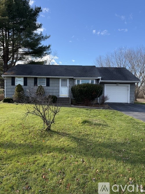 A house with a grey roof and a white garage door is surrounded by a grassy lawn.