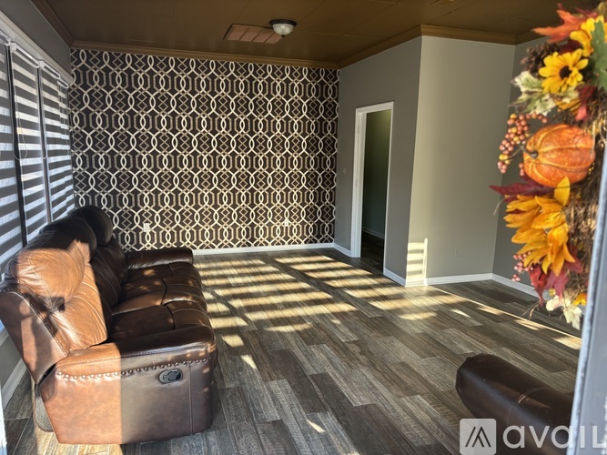 A living room with a brown leather couch and a patterned wallpaper.