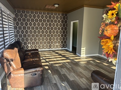 A living room with a brown leather couch and a patterned wallpaper.