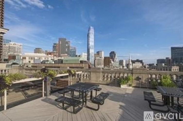 A rooftop patio with picnic tables and benches overlooking a city skyline.