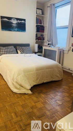 A bedroom with a bed, a window with curtains, a fan, and a painting on the wall.