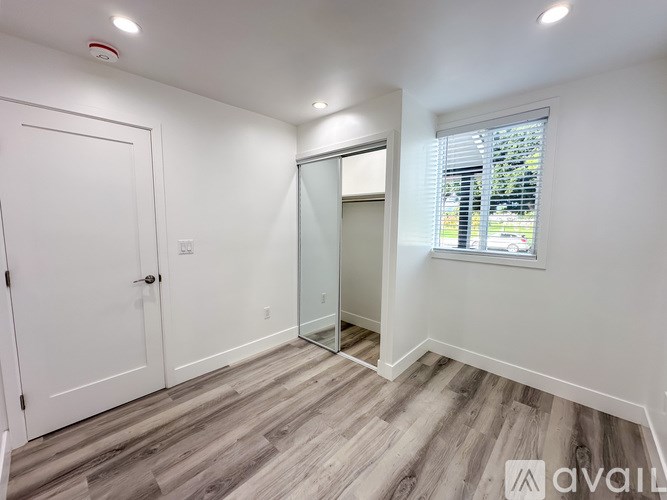 A room with a white door, a window with blinds, and a wooden floor.