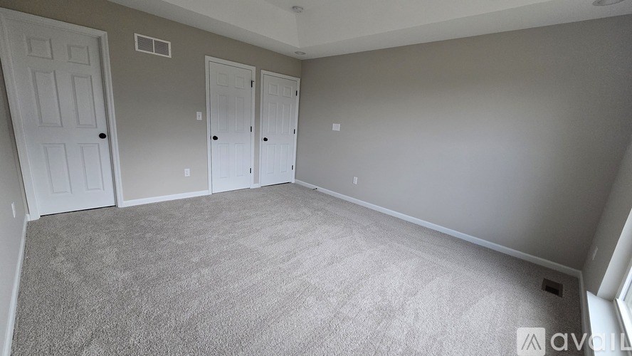 A room with grey carpet and three white doors.