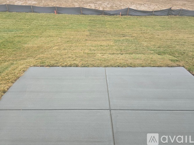 A concrete slab is in the foreground with a grassy field and a fence in the background.