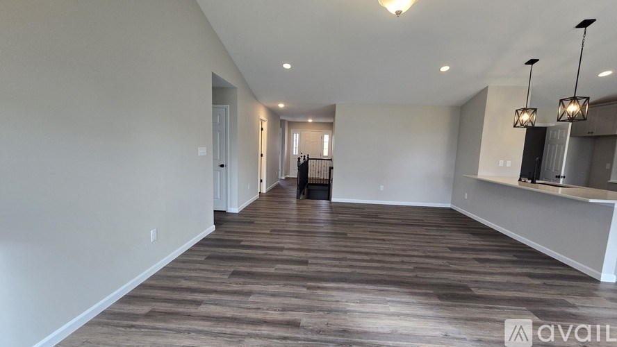 A spacious room with wooden flooring and a long hallway leading to a door.