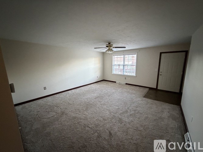 A room with a carpeted floor, a ceiling fan, and a window with blinds.