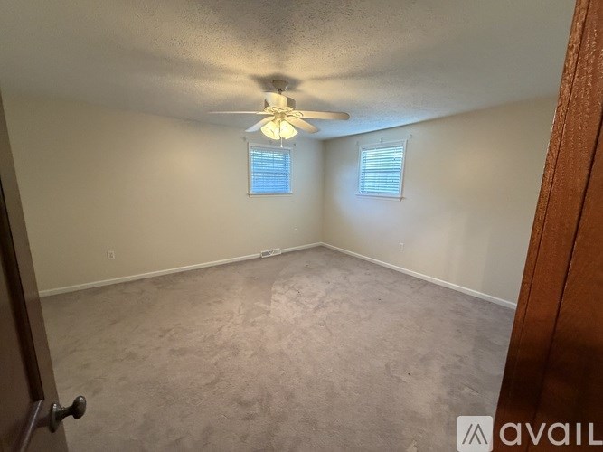 A room with a ceiling fan and two windows.