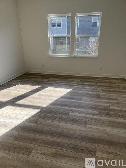A room with wooden flooring and two windows.