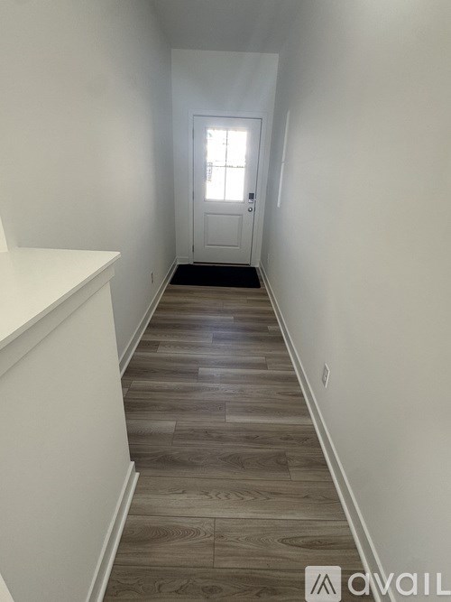 A hallway with wooden floors and white walls leading to a door.