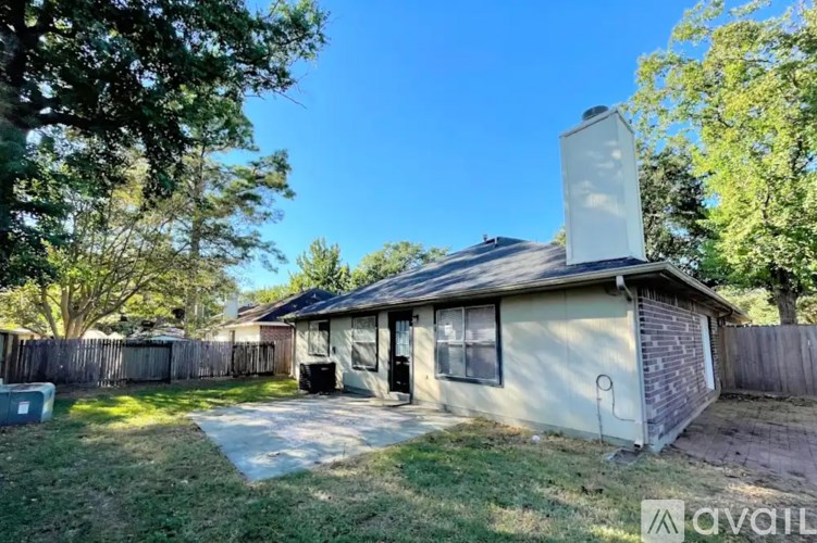 A house with a chimney is surrounded by a fence and trees.