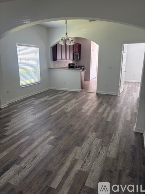 A room with wooden flooring and a kitchen area in the background.