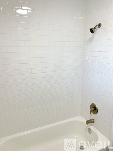 A white tiled bathroom with a white bathtub and a shower head.