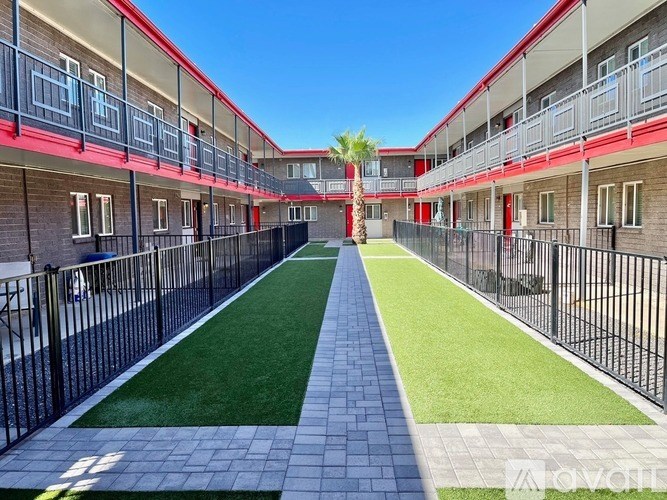 A long, narrow courtyard with a green lawn and brick walkway separates two rows of red and white apartment buildings.