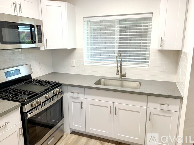 A kitchen with a stove, sink, and cabinets.
