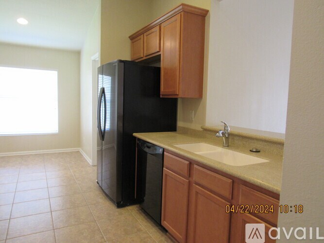 A kitchen with a black refrigerator, brown cabinets, and a white sink.