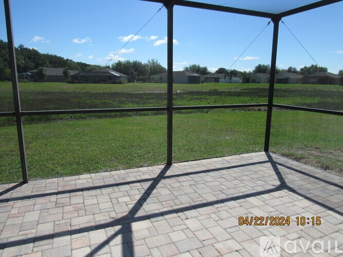 A patio with a brick floor and a metal frame in the foreground with a view of a green field and houses in the background.