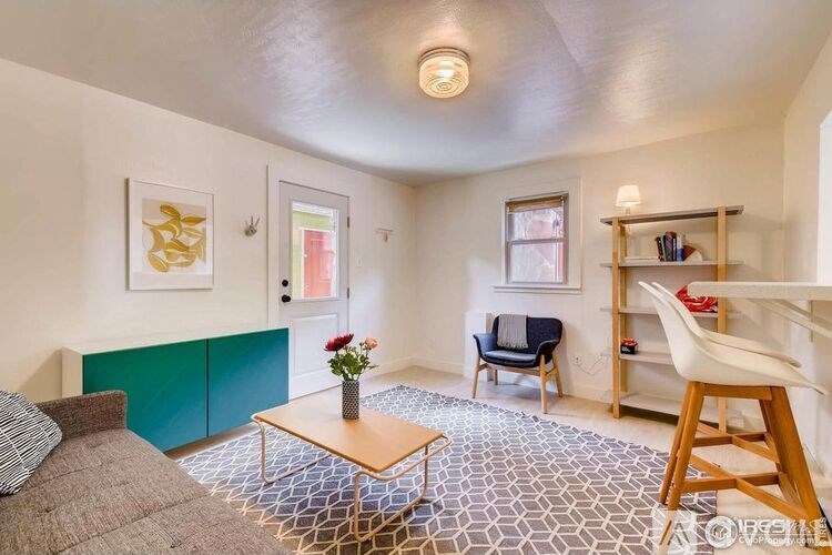 A living room with a grey couch, a wooden coffee table, a blue cabinet, a white chair, a bookshelf, and a painting on the wall.