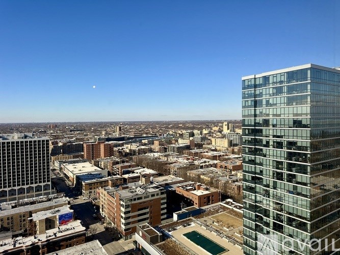 A cityscape with a tall glass building in the foreground and a clear blue sky above.