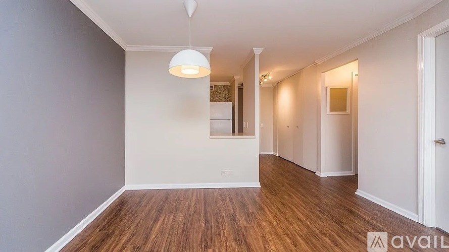 A room with wooden floors and white walls, with a hanging light fixture and a door on the right.