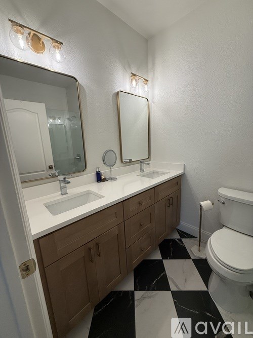 A bathroom with a sink, mirror, toilet and a black and white checkered floor.