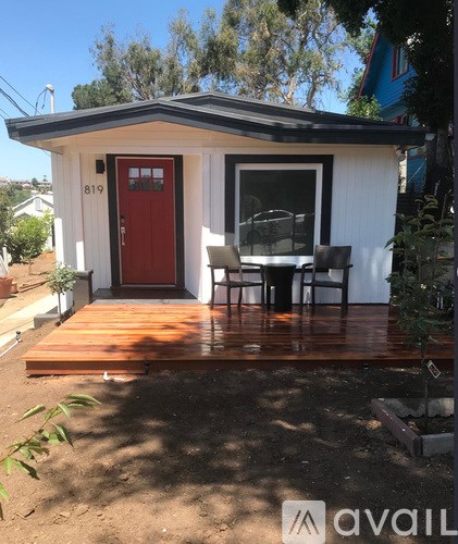 A small white house with a red door and a wooden deck.