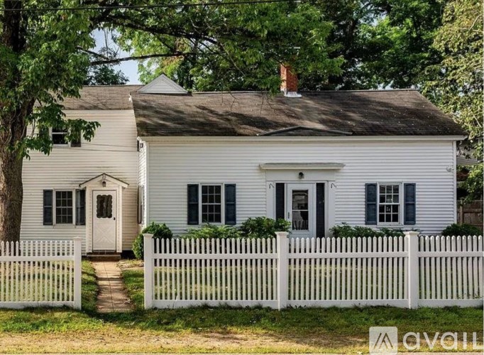 A white house with a grey roof and a white picket fence.