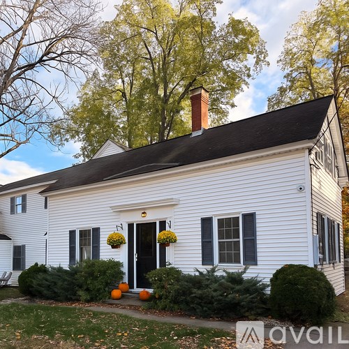 A white house with a black door and windows with flowers hanging on the door.