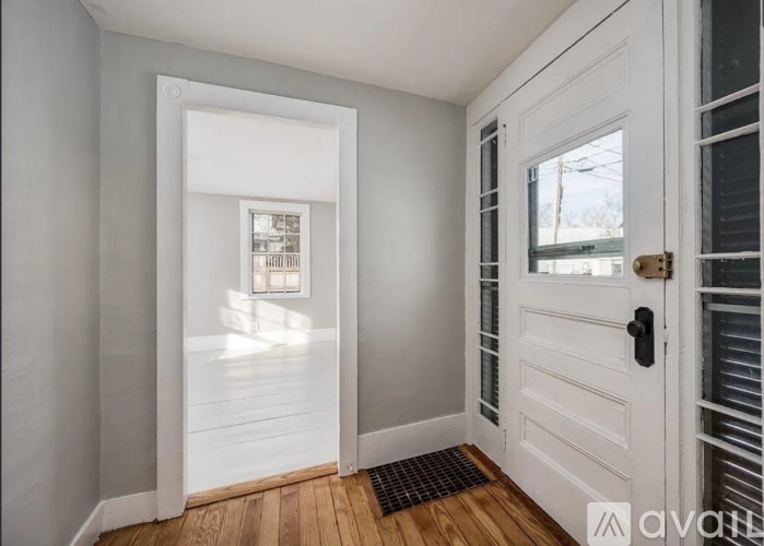 A white door with a black handle is open to a room with a window.
