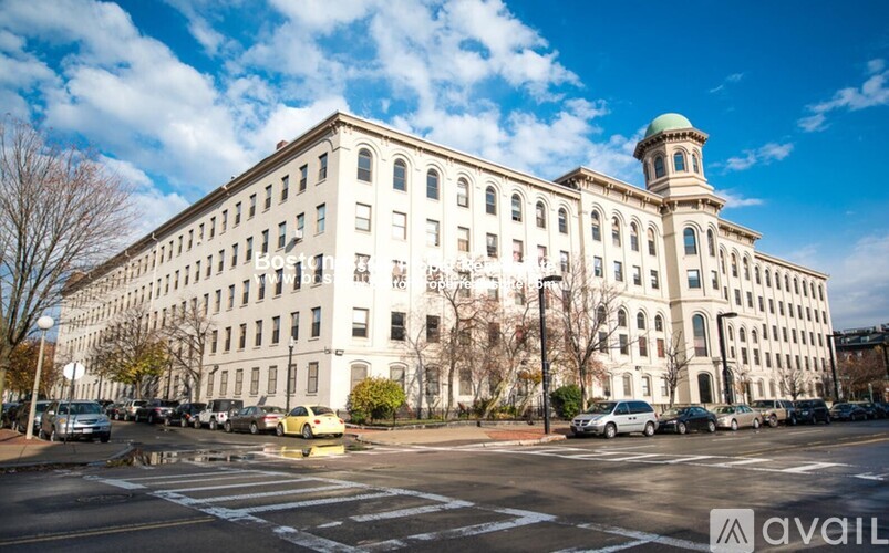 A large white building with a green dome on top is surrounded by parked cars.