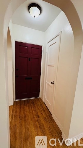 A hallway with a red door and wooden floors.