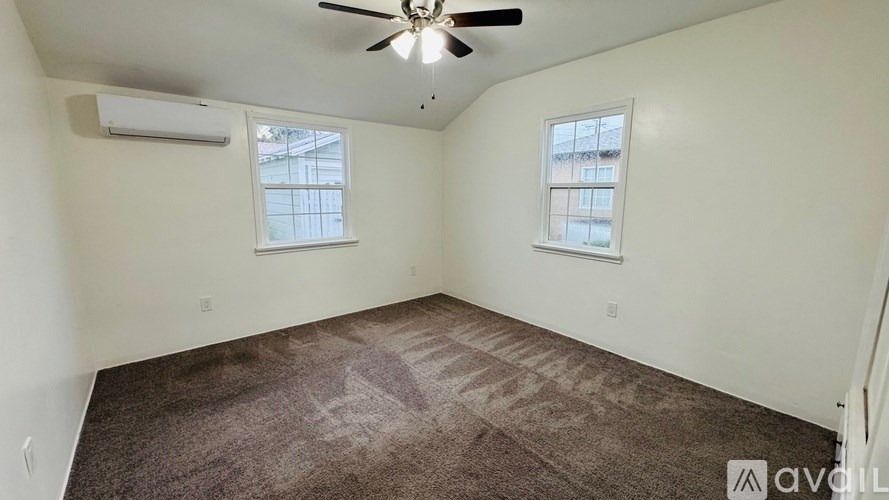 A room with a carpeted floor, a ceiling fan, and two windows.