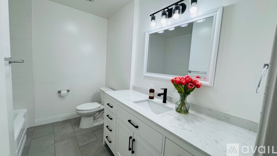 A bathroom with a white countertop and a vase of red flowers.